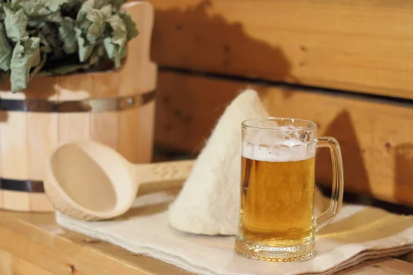 A mug of light beer and bath accessories are in the interior of the Russian bath.