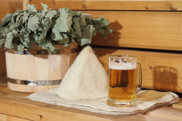 A mug of light beer and bath accessories are in the interior of the Russian bath.