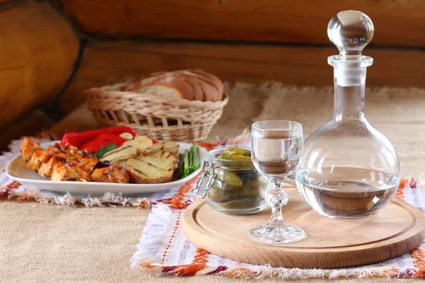 Bir bardak votka ve masada sıcak yemek. Bir bardak votka ve bir tabak tavuk kebap, ızgara patates ve sebze.