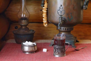 Masanın üzerinde eski bir semaver ve lambanın yanında bir bardak siyah çay var.. 