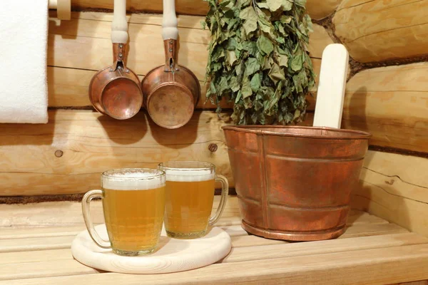 Two glass mugs of light beer in the interior of sauna among copper accessories.