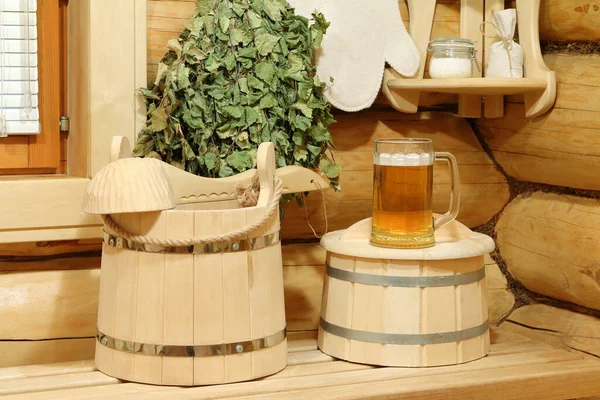 Mug of cold light beer on the wooden barrel and sauna accessories.