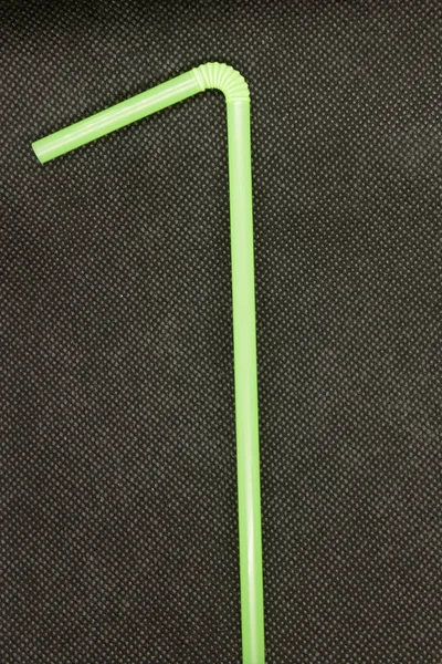 This is a photograph of a Neon Green plastic straw isolated on a textured Black background