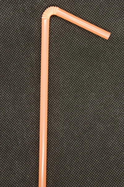 This is a photograph of a Neon Orange plastic straw isolated on a textured Black background