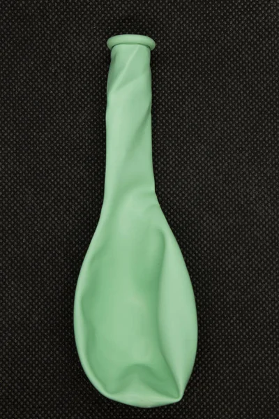 This is a photograph of a Green deflated balloon isolated on a textured Black background