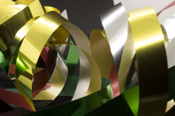 This is a photograph of Gold,Silver,Green and Red Metallic Ribbons placed infront of a Black background