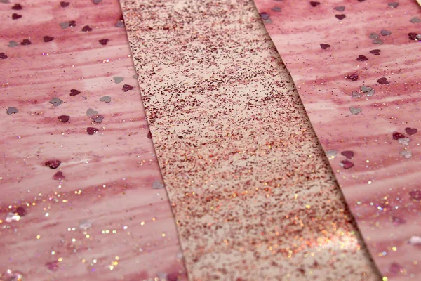 This is a photograph of an abstract background created by organizing stripes created using pink glitter paint and heart sequins