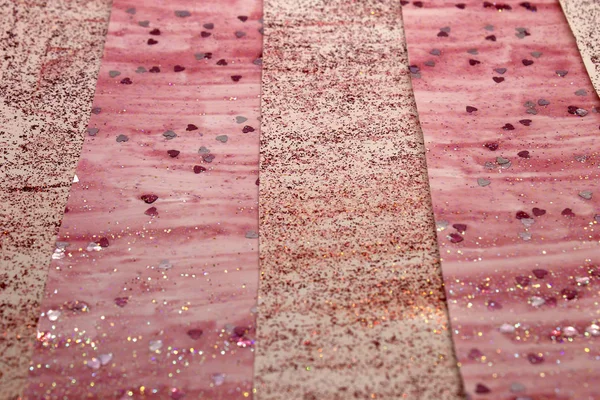 This is a photograph of an abstract background created by organizing stripes created using pink glitter paint and heart sequins
