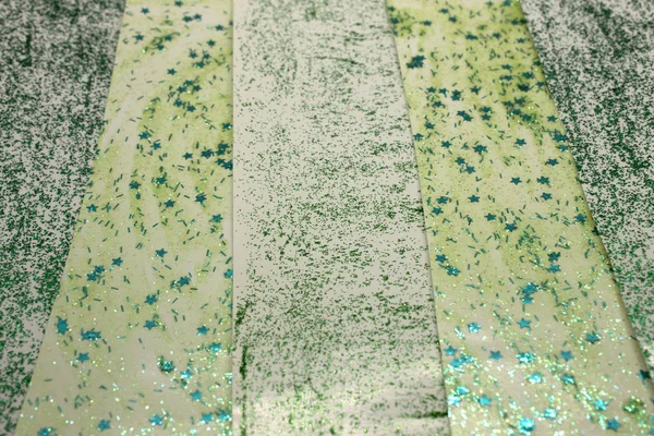 This is a photograph of an abstract background created by organizing stripes created using light and dark Green glitter paint and star sequins