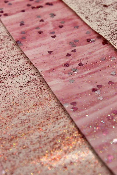 This is a photograph of an abstract background created by organizing stripes created using pink glitter paint and heart sequins