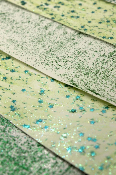 This is a photograph of an abstract background created by organizing stripes created using light and dark Green glitter paint and star sequins