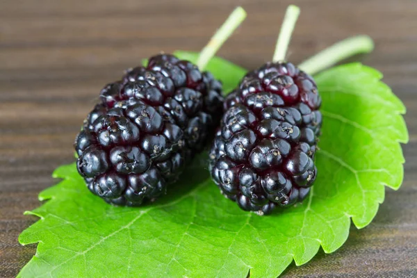 Group of black mulberries with a leaf on the dark brown background. Closeup. — Stock Photo, Image