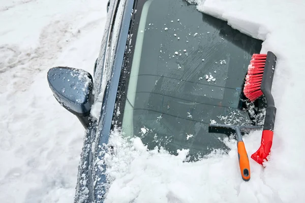 Raschietto di ghiaccio e spazzola per la pulizia dell'automobile è sul cofano della macchina. Neve che rimuove dalla macchina dopo la bufera di neve. Parzialmente pulito parabrezza. — Foto Stock