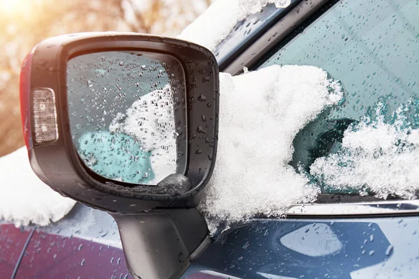 Woda i śnieg w samochodzie po śnieżycy. Krople wody na boczne lusterko wsteczne. Śnieg topnieje po opadach śniegu w mieście. — Zdjęcie stockowe