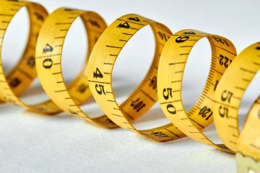 Beyaz zemin üzerinde uzunluk ve genişlik ölçümü için siyah şekilli sarı renkli santimetre. Tasarımınız için terzinin şeridini ölçüyorum. Yakın çekim, seçici odaklanma