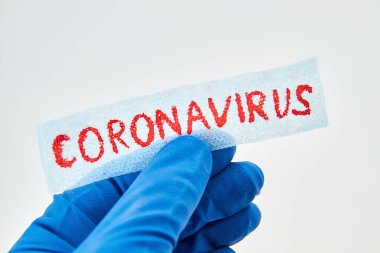 Mavi tıbbi eldiven, beyaz arka planda Coronavirus yazısını tutuyor..