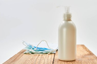 Sıvı sabun makinesi ve ahşap arka planda mavi tıbbi koruyucu maskeler. Covid-19 'dan korunmak için hijyen. Coronavirus önleme.