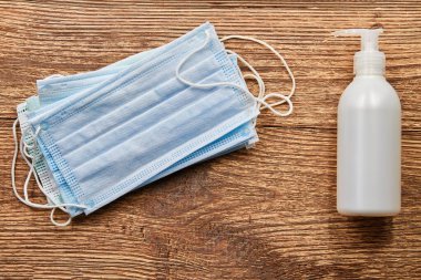 Sıvı sabun makinesi ve ahşap arka planda mavi tıbbi koruyucu maskeler. Covid-19 'dan korunmak için hijyen. Coronavirus önleme.