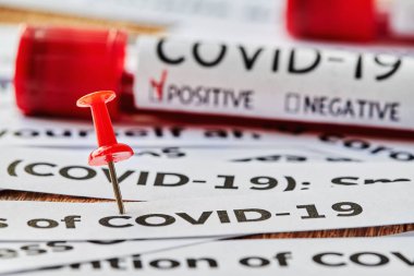 Coronavirus gazetesinin manşetlerinde kırmızı raptiye vardı. Üzerinde COVID-19 için kan testi tüpü ve arka planda pozitif işaret vardı. Yakın çekim, seçici odaklanma