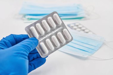 Mavi koruyucu eldivenli bir el haplarla su toplayabilir. Tıbbi koruyucu maskeler, arka planda haplar. Viral hastalık önleme kavramı.