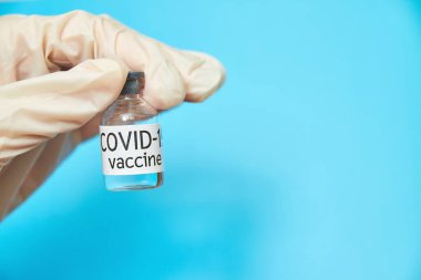 Kavramsal görüntü. Koruyucu eldivendeki bir el Covid-19 için aşı taşıyor. Sağlık ve tıbbi konsept. Yakın plan, mavi arkaplan.