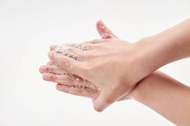 Coronavirus veya Covid-19 konsepti. Küçük bir kız ellerini sabunla yıkıyor. Beyaz arka planda sabunla el yıkama işlemi. Yakın çekim, seçici odaklanma