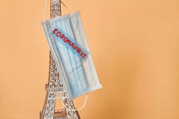 Quarantine concept. Model of the Eiffel Tower with a medical mask on it with the inscription coronavirus.