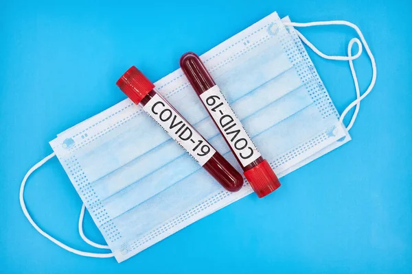 Kavramsal fotoğraf. Coronavirus için kan testi örnekleri. Yüzün koruyucu maskelerinde kan örnekleri olan tüpler. Mavi arkaplan