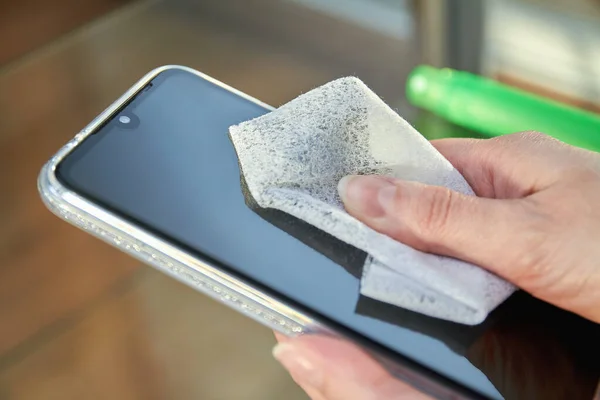 Woman is cleaning a smartphone with a jet of alcohol aerosol hand sanitizer and disposable cloth at home. Precautions regarding viruses