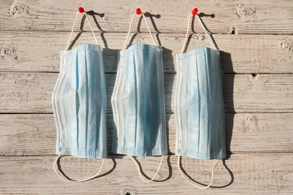 Kovid 19 virüs enfeksiyonunu önlemek için maskeler, tıbbi koruyucu maskeler. Ahşap bir arka planda üç maske asılı. Sağlık ve tıbbi konsept. Yaklaş, sert güneş ışığı.