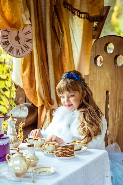 Vista frontal de uma menina bonita na paisagem de Alice no País das Maravilhas segurando uma xícara de chá na mesa — Fotografia de Stock
