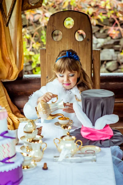 Vista frontal de uma menina bonita na paisagem de Alice no País das Maravilhas derramando chá em uma xícara na mesa — Fotografia de Stock