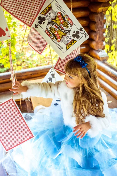 An little beautiful girl playing and dancing with large playing cards on the table