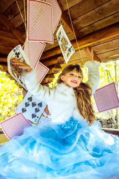 An little beautiful girl playing and dancing with large playing cards on the table