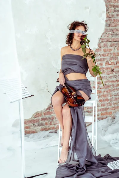 Hermosa mujer sosteniendo un violín y oliendo rosa roja — Foto de Stock