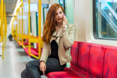 Kız boş bir metroyu içinde cep telefonuyla konuşuyor. Kız bir akıllı telefon ile metro bir arabada oturuyor