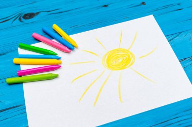 Boyalı güneş ile çok renkli kalemler yan görünüm mavi ahşap arka plan üzerinde beyaz kağıt üzerinde