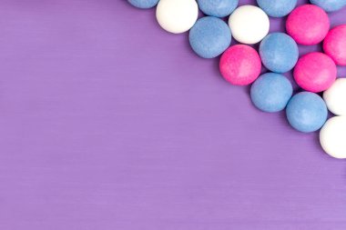 Ahşap mor zemin üzerine üstten görünüm sağ üst köşesinde kare renkli Çikolata kaplamalı şeker. Kopya alanı