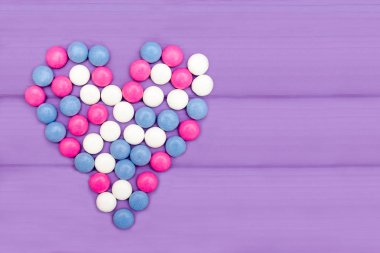 Şekerler farklı renklerde mor bir arka plan üzerinde bir kalp oluşturan