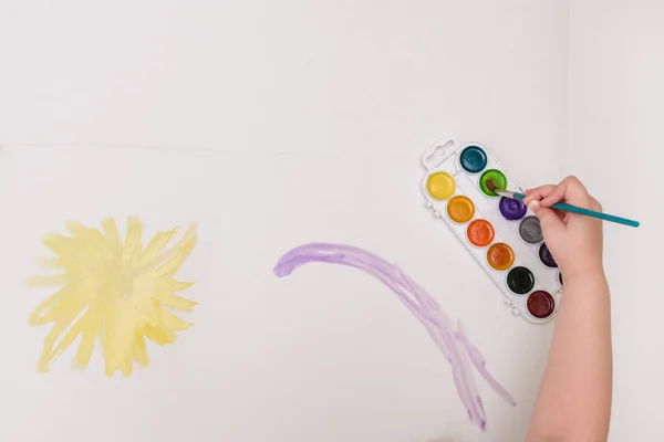 Mano infantil con pinceles dibujo sobre papel blanco sol amarillo —  Fotos de Stock