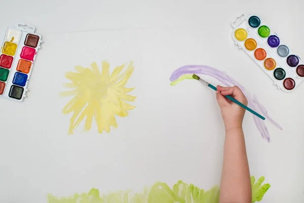 Main d'enfant avec dessin au pinceau jaune soleil sur papier blanc — Photo