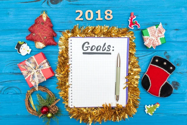Cuaderno con objetivos de año nuevo para 2018 con un bolígrafo y números 2018, cajas de regalo y adornos de Año Nuevo en una mesa de madera azul — Foto de Stock