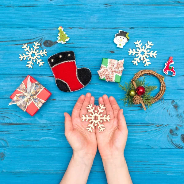 Ημερολόγιο Χριστουγέννων σε άσπρο φόντο. Γυναικεία χέρια που κρατούν χριστουγεννιάτικο ξύλινο νιφάδες χιονιού κοντά κουτιά δώρων και το νέο έτος στολίδια για μπλε παλιό τραπέζι — Φωτογραφία Αρχείου