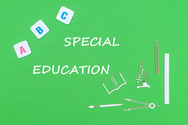 Text special education, from above wooden minitures school supplies and abc letters on green background — Stock Photo, Image