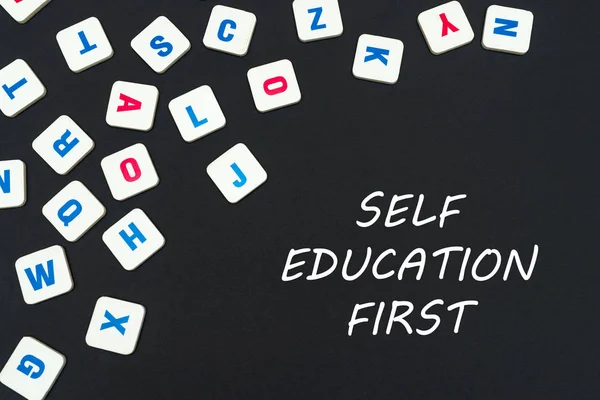 Inglês colorido letras quadradas espalhadas no fundo preto com texto auto-educação primeiro — Fotografia de Stock
