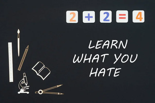 Material escolar colocado sobre fondo negro con texto aprende lo que odias — Foto de Stock
