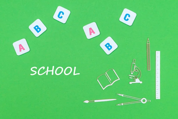 Text school, from above wooden minitures school supplies and abc letters on green background — Stock Photo, Image