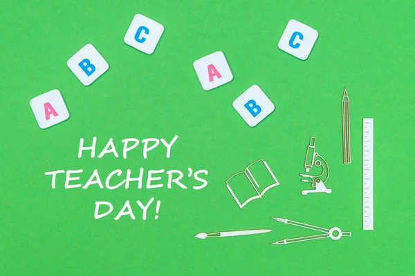 Dzień szczęśliwy tekst nauczyciela, z góry minitures drewniane przybory szkolne i litery abc na zielonym tle — Zdjęcie stockowe