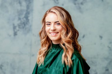 Gri arkaplanda mükemmel kıvırcık saç stili ve makyajı olan güzel, gülümseyen beyaz, sarışın bir kadının portresi..