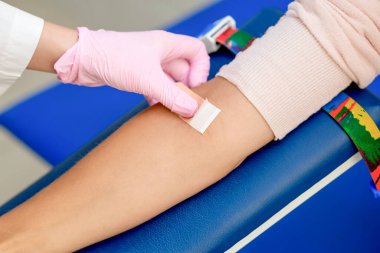 Kauçuk koruyucu eldivenli doktor kan örneği aldıktan sonra koluna yapıştırıcı yapıştırıyor..